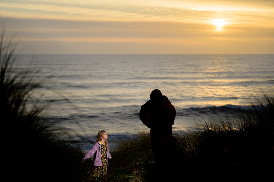 A model posing on the beach at sunset with a camera assistant holding the Neewer Q4 flash as a photograph is being taken.