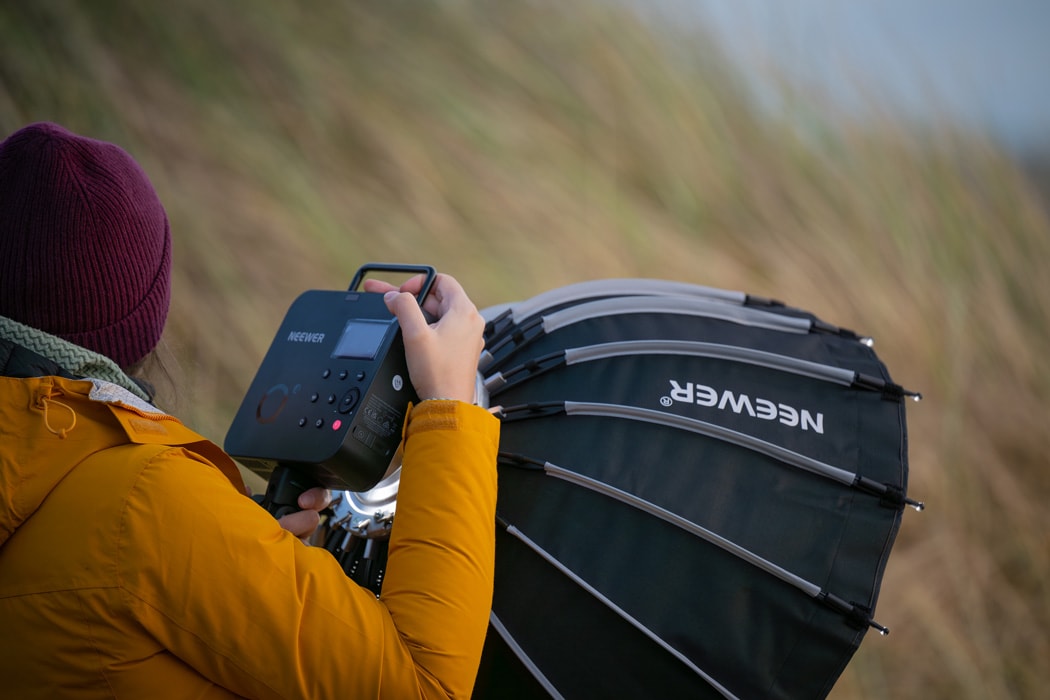 A woman holding the Neewer Q4 flash strobe while on the beach at a photoshoot.