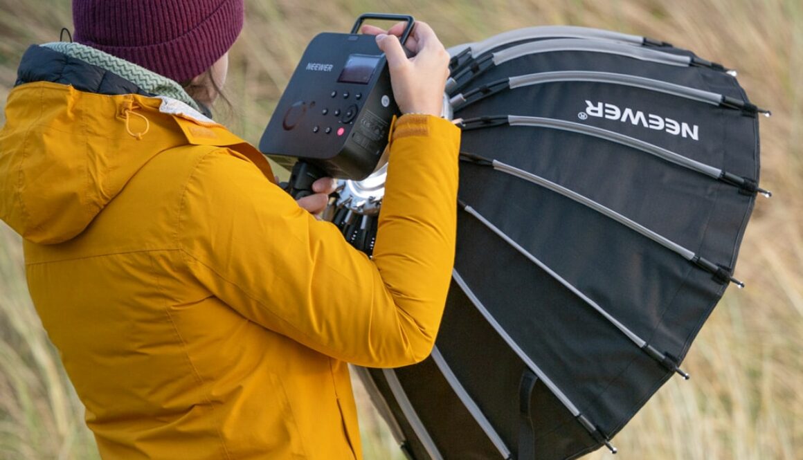 A woman holding the Neewer Q4 flash strobe while on the beach at a photoshoot.