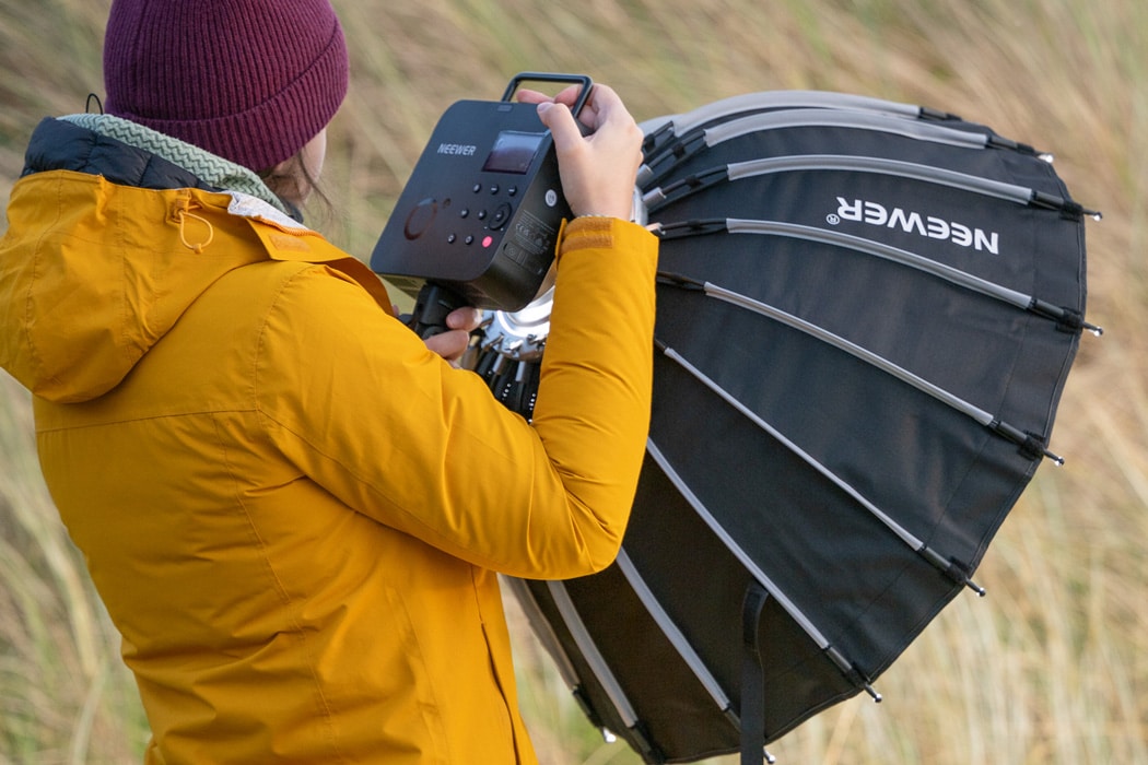 A woman holding the Neewer Q4 flash strobe while on the beach at a photoshoot.